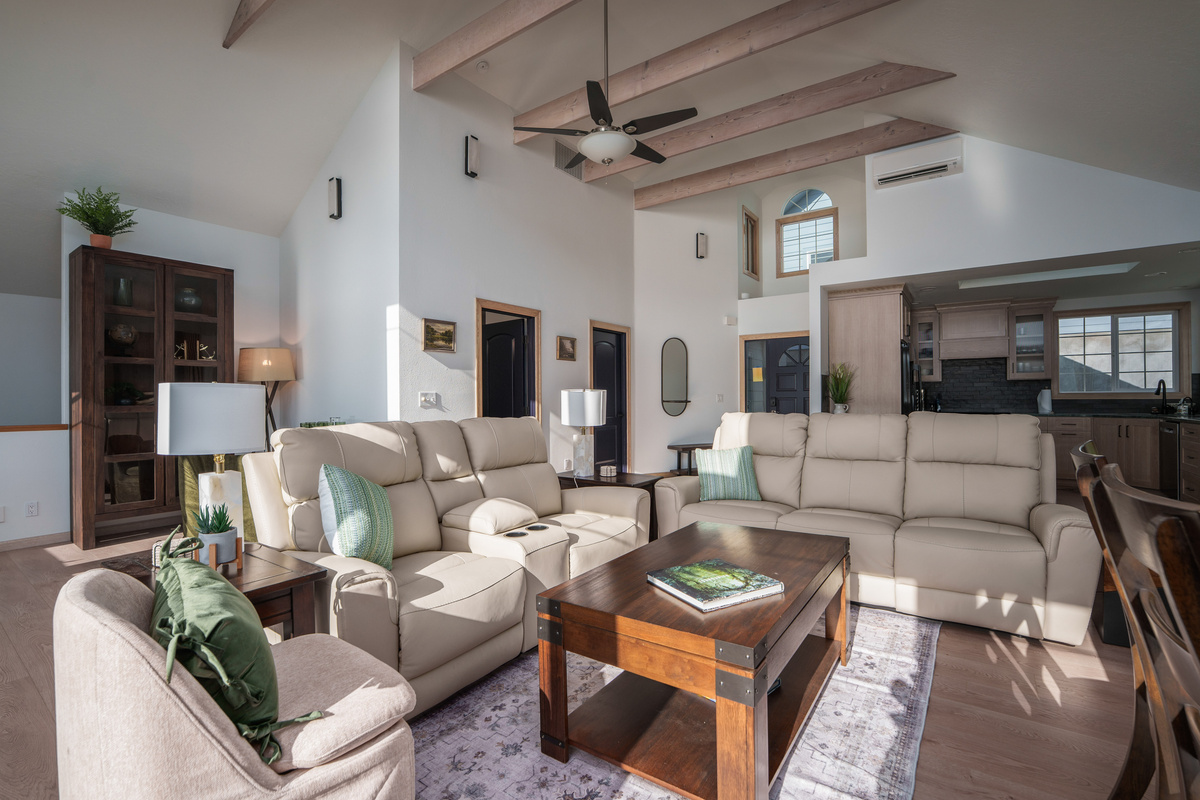 Bright, inviting living room with vaulted ceilings, exposed wood beams, comfortable seating, and plenty of space for the whole group to relax together. Coffee table converts into a laptop-friendly working station.
