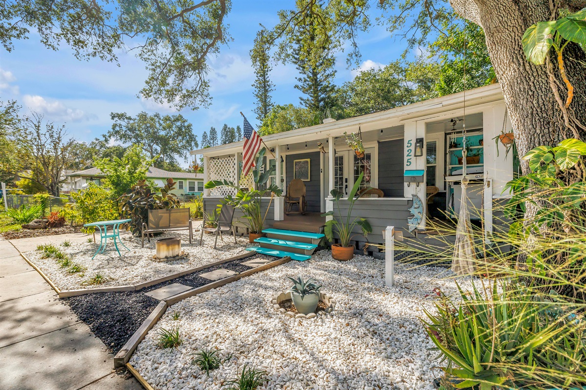 Charming exterior with a welcoming front porch, landscaped yard, outdoor seating, and a peaceful garden-style setting.