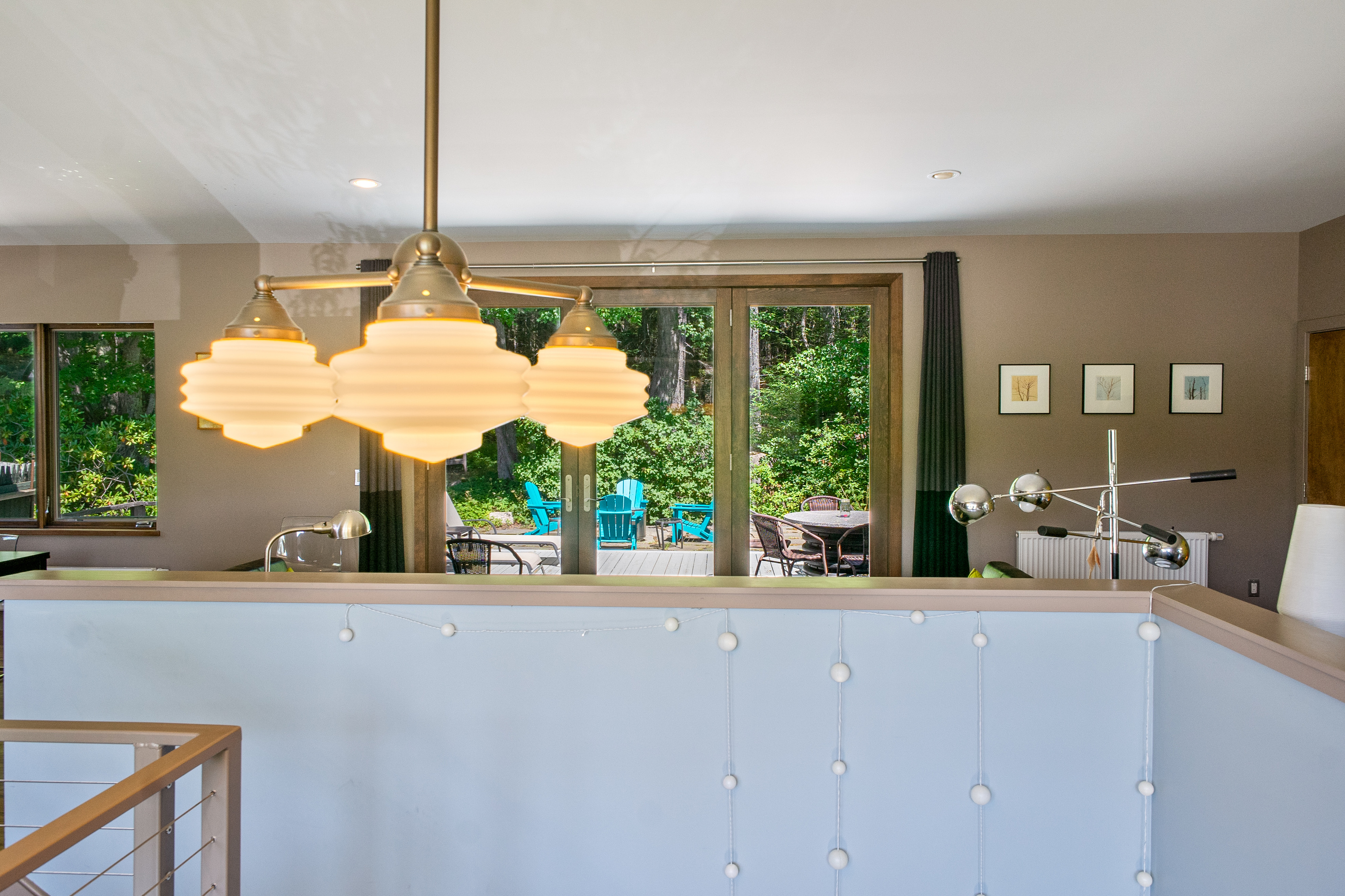 Modern designer lighting over the main stairway, framed by large picture windows and a direct-access door to the 33ft "Park Border" deck. This bright transition offers a seamless indoor-outdoor flow at the edge of Acadia National Park.