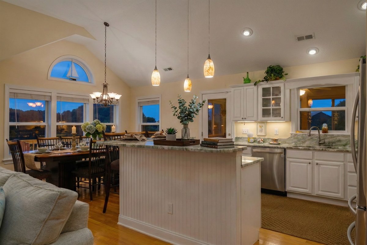 A sun-filled, open-concept kitchen and dining area featuring stainless steel appliances, a spacious breakfast bar, and a large dining table for group meals.