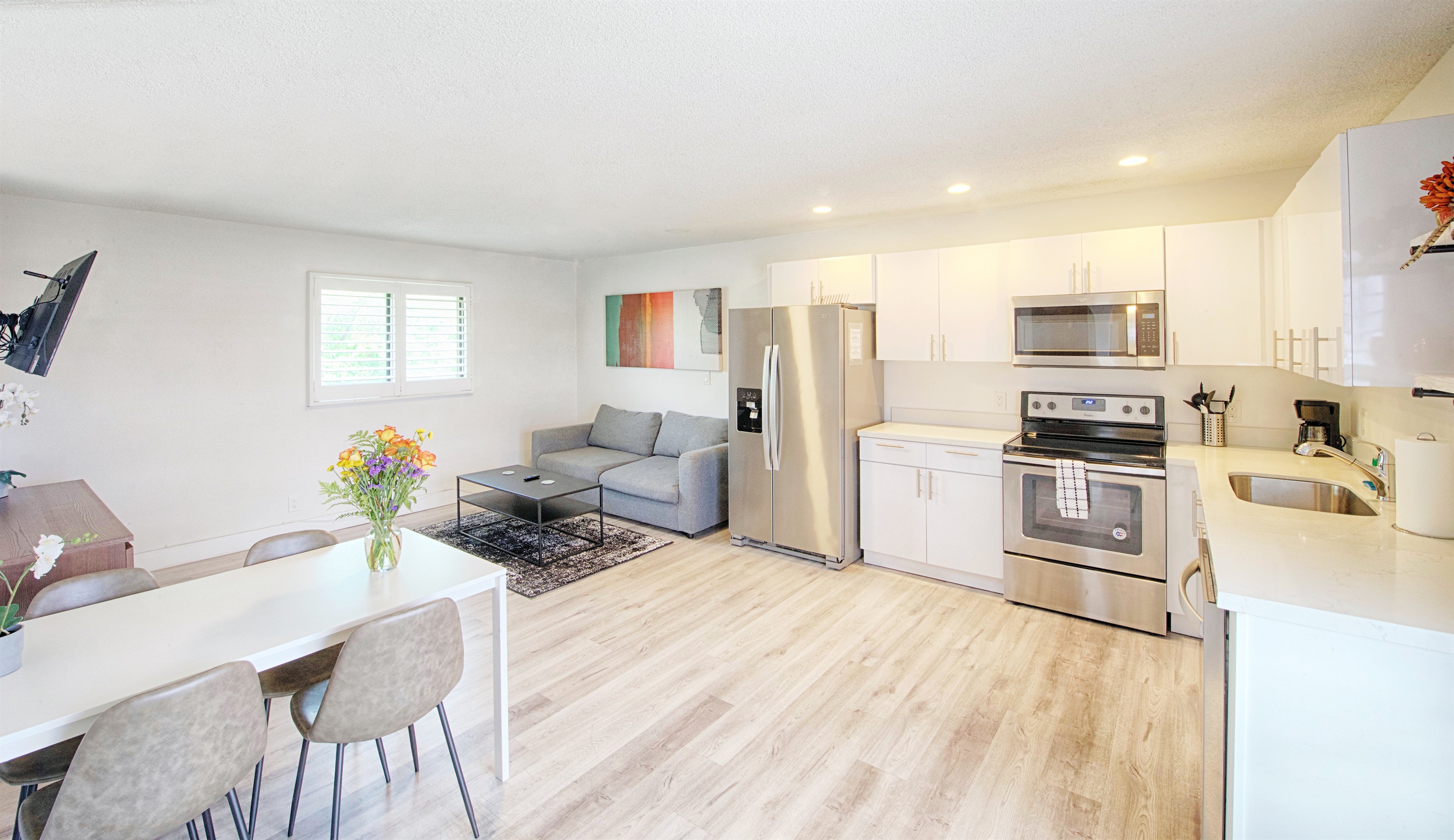 Entry way wide view showing updated kitchen with white quartz counters, deep sink and SS appliances. Fridge includes auto ice maker.