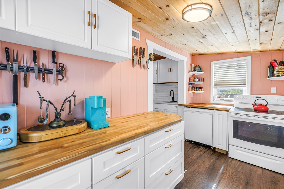 Bright kitchen with white cabinetry, butcher block countertops, stainless steel appliances, and charming wood ceiling details.