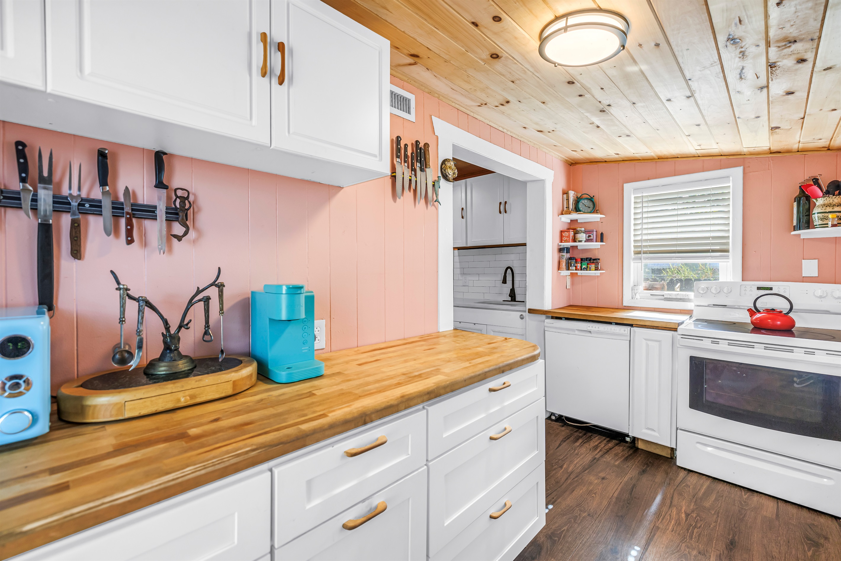 Bright kitchen with white cabinetry, butcher block countertops, stainless steel appliances, and charming wood ceiling details.