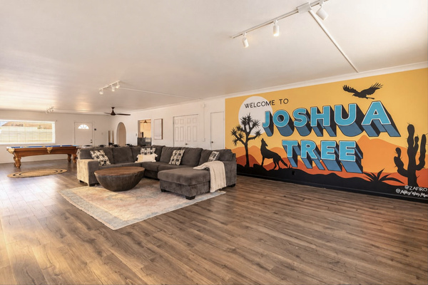 Open living room with a wall-size Joshua Tree mural, sectional sofa and pool table