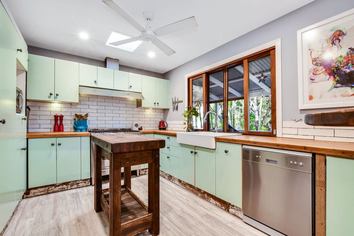 Timber-framed windows bring lush garden greenery into view from the kitchen at Aaron's Beachside Boat House, creating a bright connection to the tropical surrounds.