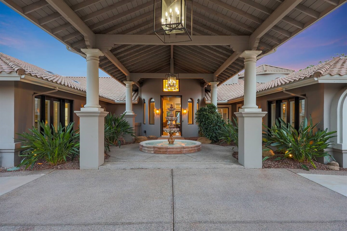 The front courtyard invites you in with ambient lighting, tropical greenery, and timeless Southwestern architecture.

