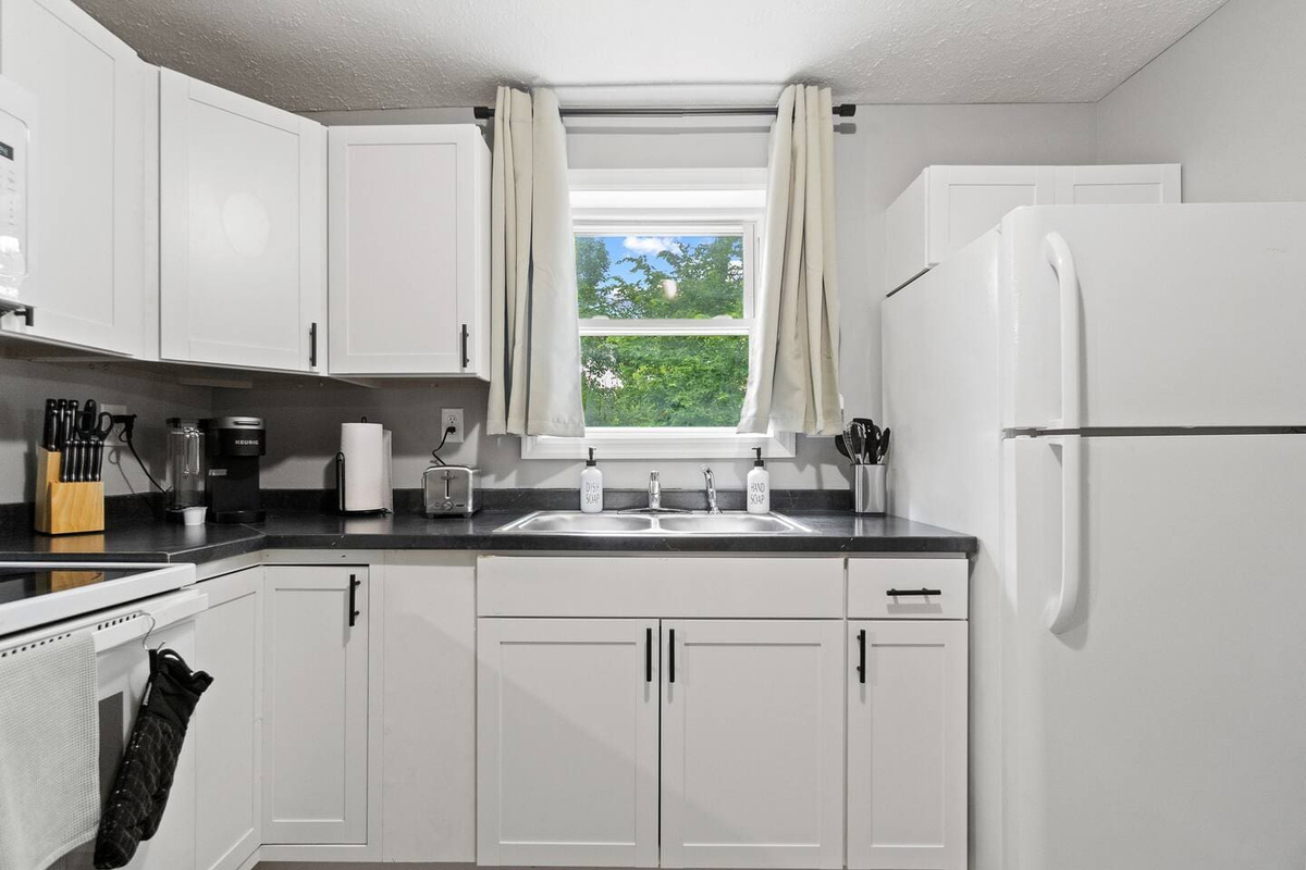 Well-equipped kitchen featuring a fridge, toaster, knife set, and coffee maker, with a window offering a lovely view while you cook.