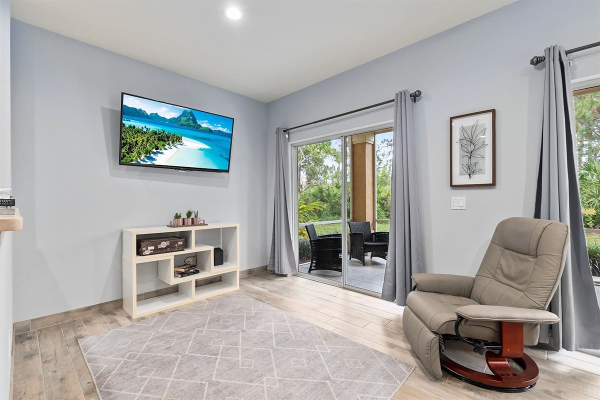 Bright living area featuring a wall-mounted TV, comfortable recliner, and direct access to the screened patio.