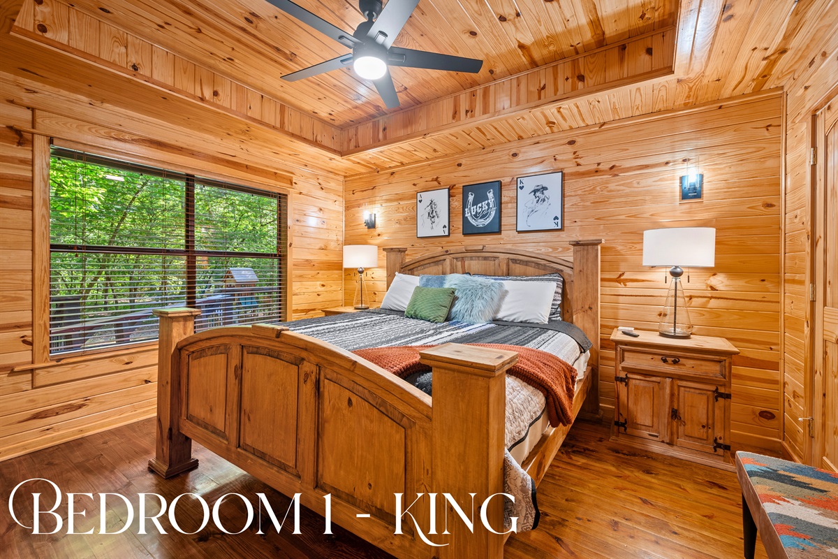 Bedroom 1 features a king-sized bed, wood furniture, and a peaceful forest view through large windows.