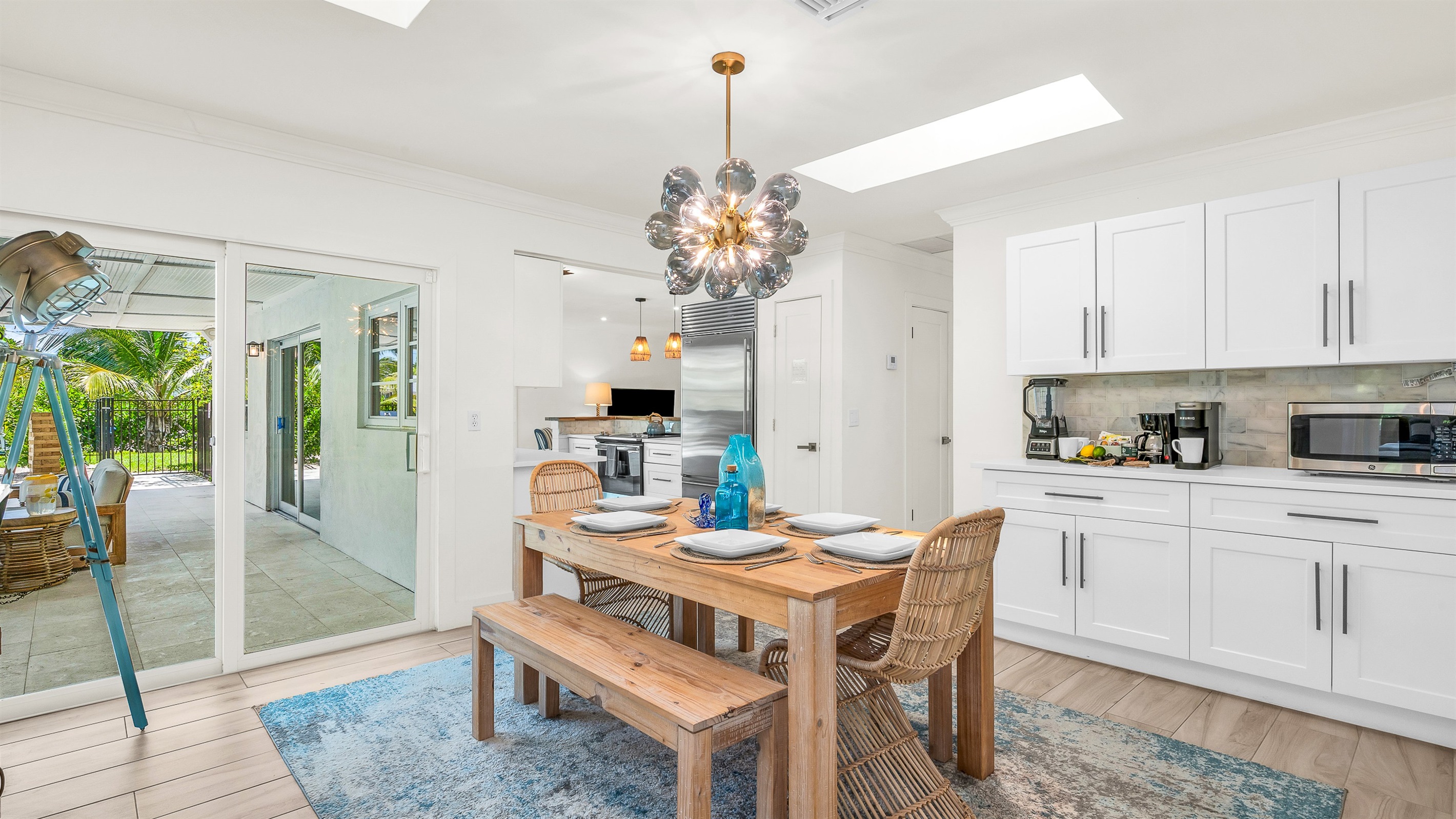 Gather around the rustic wood dining table with seating for six, accented by chic rattan chairs and a statement chandelier. Surrounded by natural light and stylish coastal décor, it’s the perfect space for enjoying meals or entertaining in style.