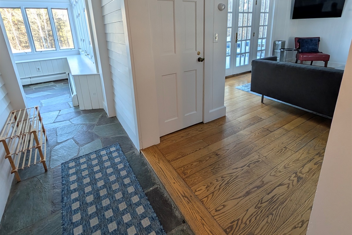 Open transition between the sunroom and living area, blending slate and hardwood floors for a warm, inviting flow.