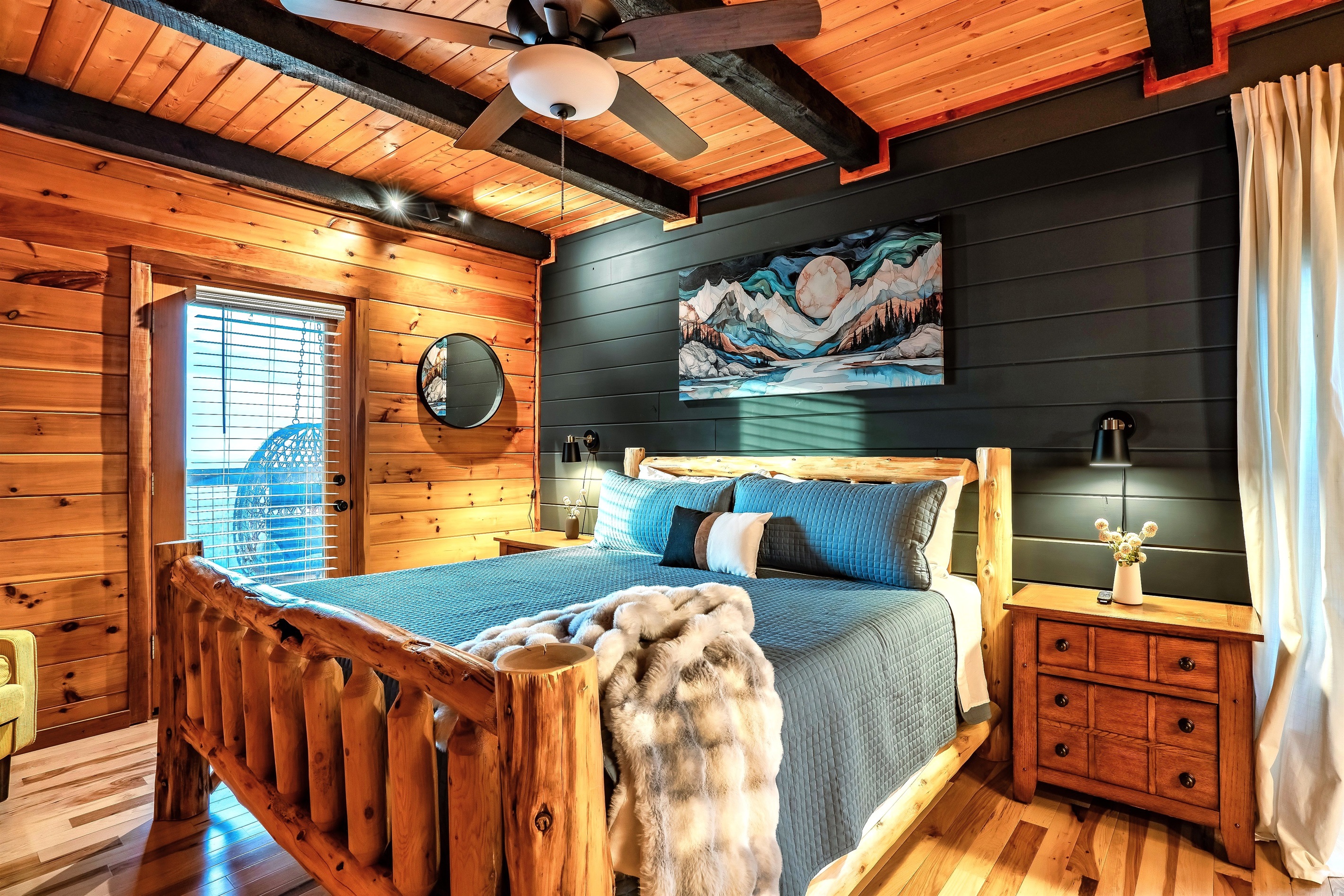 Warm and inviting master suite in a contemporary mountain cabin with darkened accent wall and direct access to the deck - specifically curated for unwinding after a day exploring the scenic outdoors.