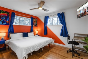 A room creatively designed with red and blue hues, equipped with a study table, TV, and adequate lighting for both work and leisure.
