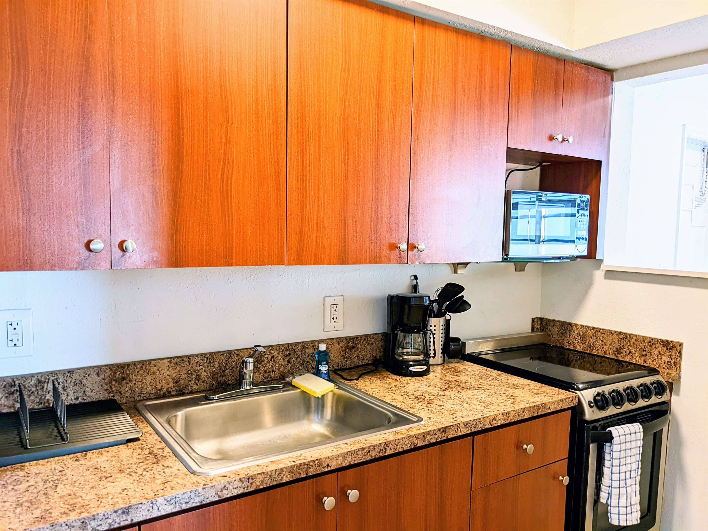 Kitchen with sink, stove and above flat range microwave.