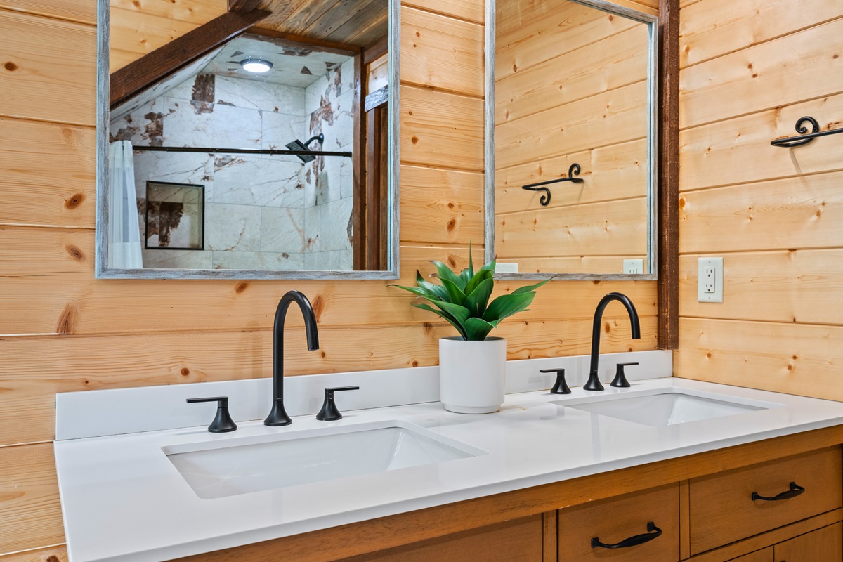 Double-sink vanity with black fixtures and wood accents.