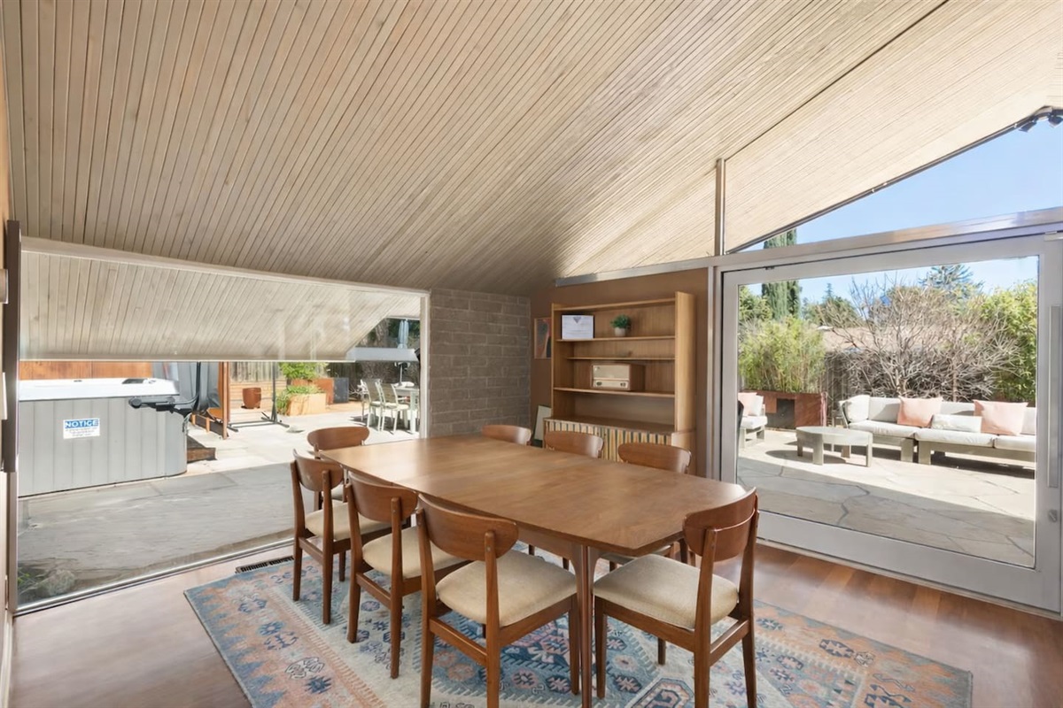Bright dining area with vaulted wood ceilings, mid-century furnishings, and seamless access to the private patio and hot tub.