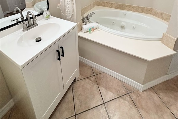 Bathroom vanity and soaking tub area with clean neutral finishes and tile flooring.