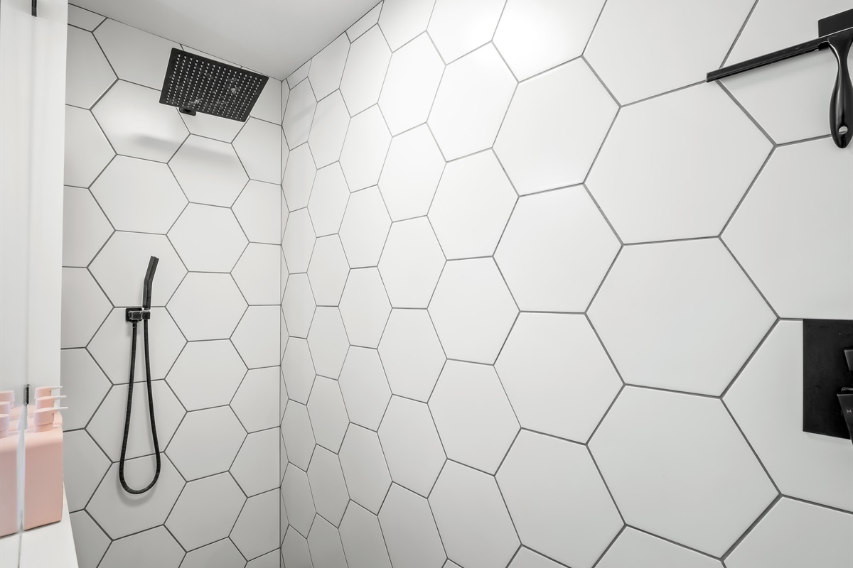 Enjoy a true spa experience with a sleek rainfall showerhead, matte black fixtures, and eye-catching oversized hex tile. Clean lines and contemporary finishes create a fresh, elevated space designed for comfort and style.