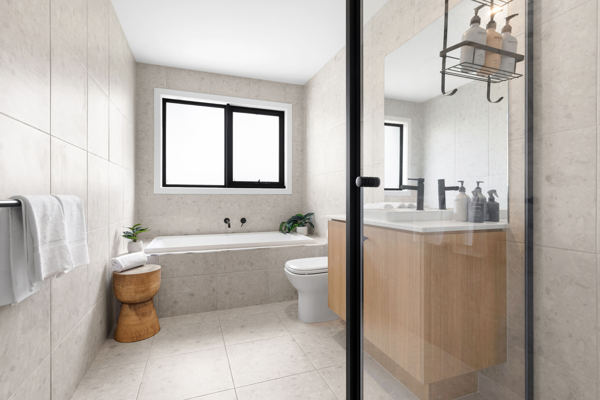 Main bathroom with a bath, glass shower screen with black frame, towel and a timber vanity.