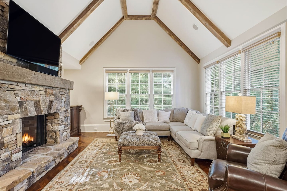 Relax in a warm and welcoming living room featuring high ceilings, a beautiful stone fireplace, and rich wood accents that create a cozy, home-like atmosphere. Enjoy a smart TV with a quality sound system perfect for movie nights and quiet mornings.