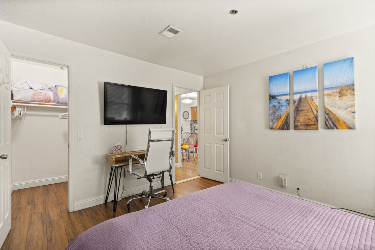 Bedroom 2 with a king bed, wall-mounted TV, desk workspace, and closet storage.
