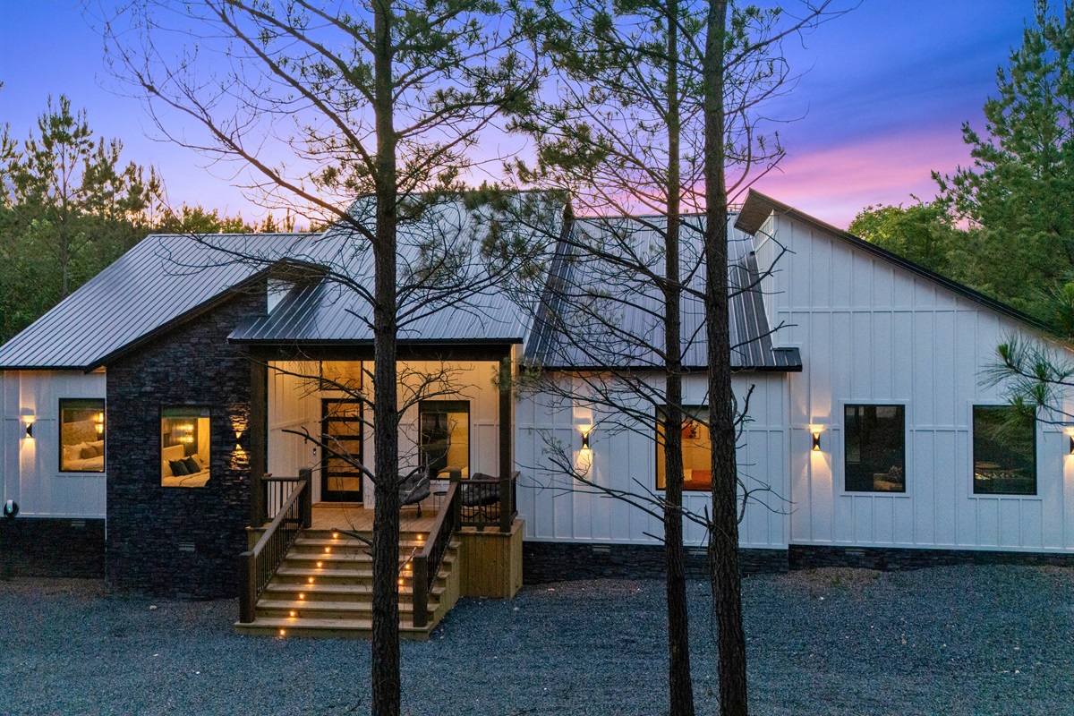 The welcoming front porch and beautifully lit exterior set the tone for a relaxing getaway surrounded by towering pines and peaceful scenery.