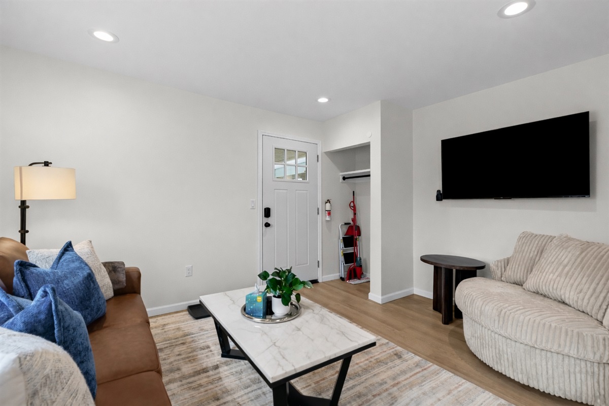 Bright, modern living room with cozy seating, smart TV, and a welcoming entryway—clean lines, warm tones, and a comfortable space to relax and unwind.