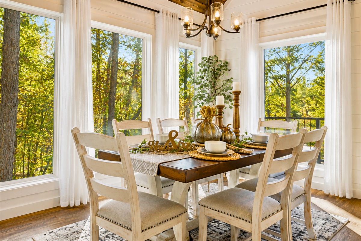 The dining space feels bright, cozy, and connected to nature with oversized windows framing the peaceful pines outside.
