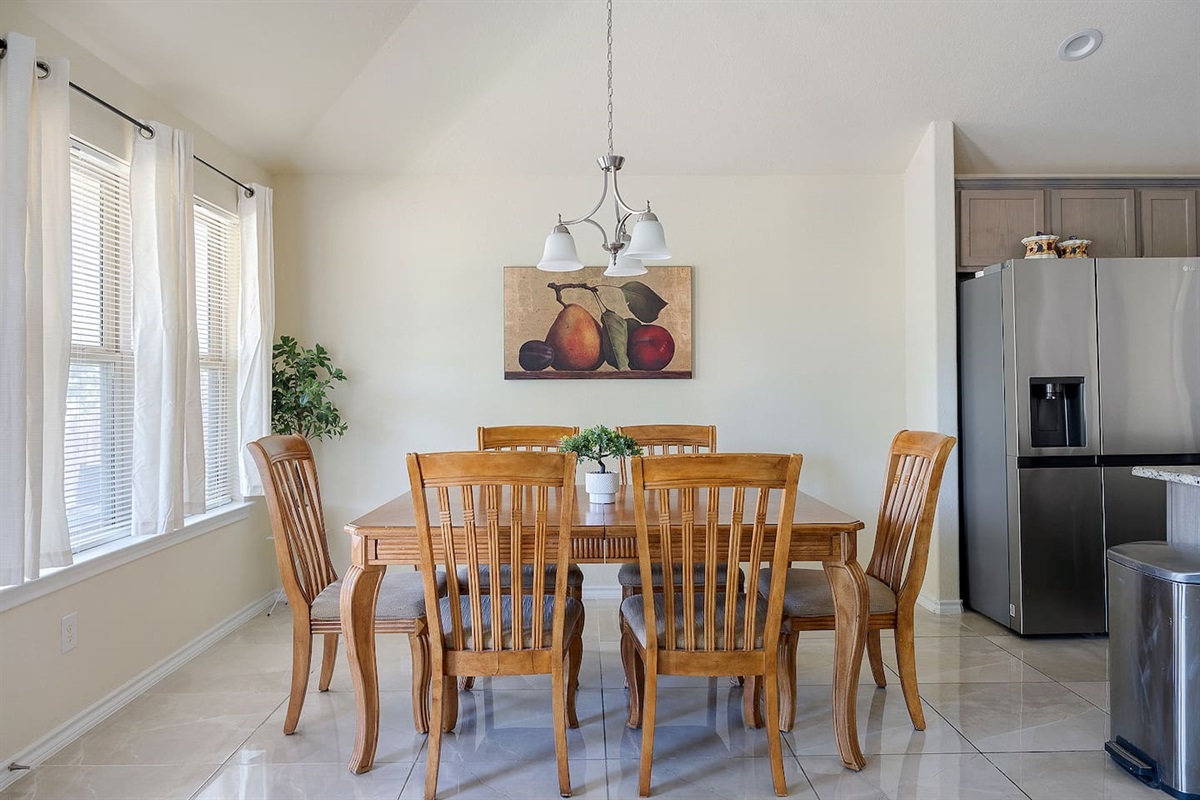 Enter to see a spacious, light-filled dining area with a classic wooden table set, tasteful lighting, and wall art.