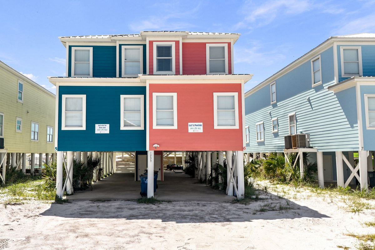 Beach house exterior featuring colorful coastal architecture, elevated living space, and a sandy walkway leading toward the home.