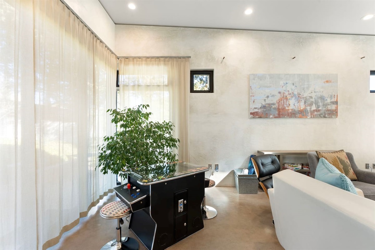 Bright lounge area with cozy seating, natural light, and a fun arcade game for added entertainment.