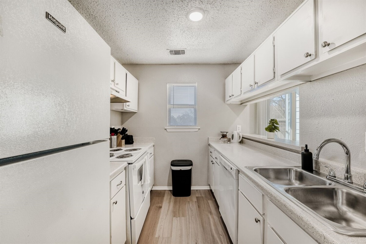 Bright galley kitchen with white cabinetry, modern appliances, and natural light.