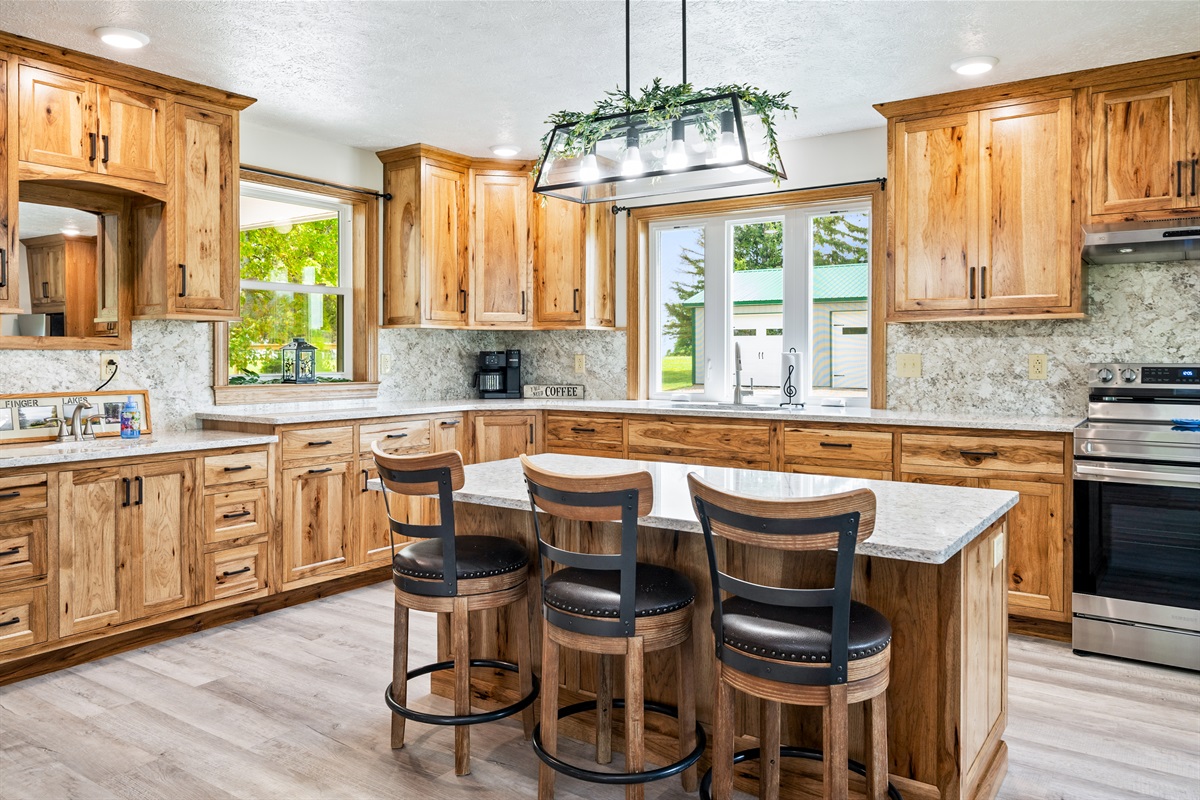 Cook in style in this fully equipped kitchen with natural wood cabinetry, granite countertops, stainless steel appliances, and a large center island with seating.