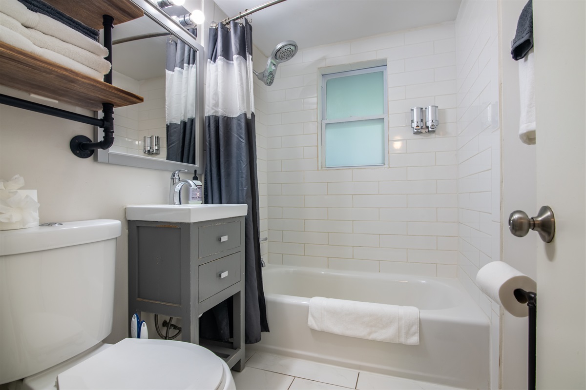 Bright full bathroom featuring a tub/shower combo, fresh towels, and sleek finishes.