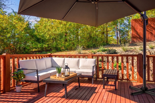 Furnished wraparound deck with luxury outdoor seating, oversized cantilever umbrella, and sweeping wooded views