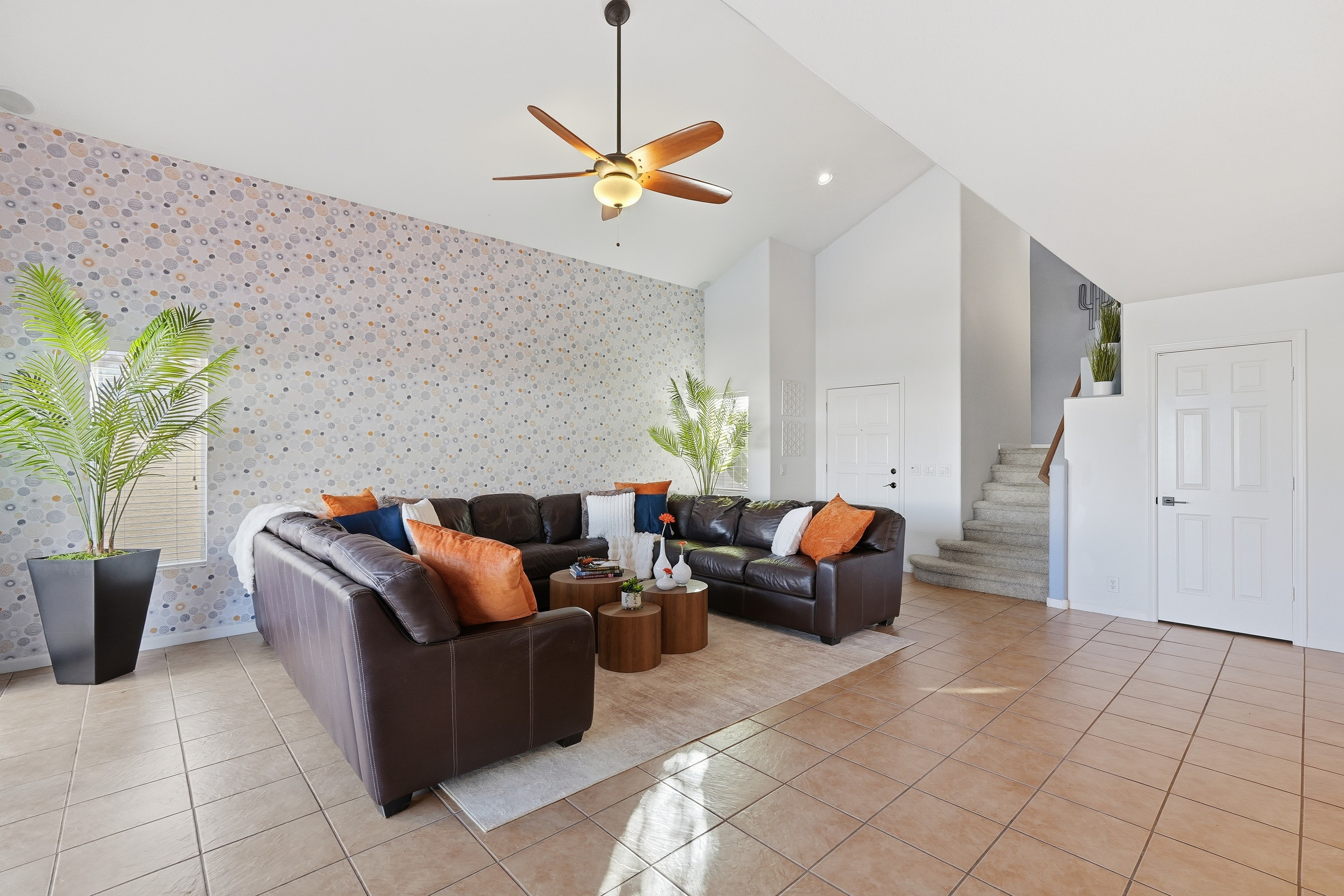 Living room with vaulted ceilings, leather sectional seating, accent wall, and open access to the staircase and main level.