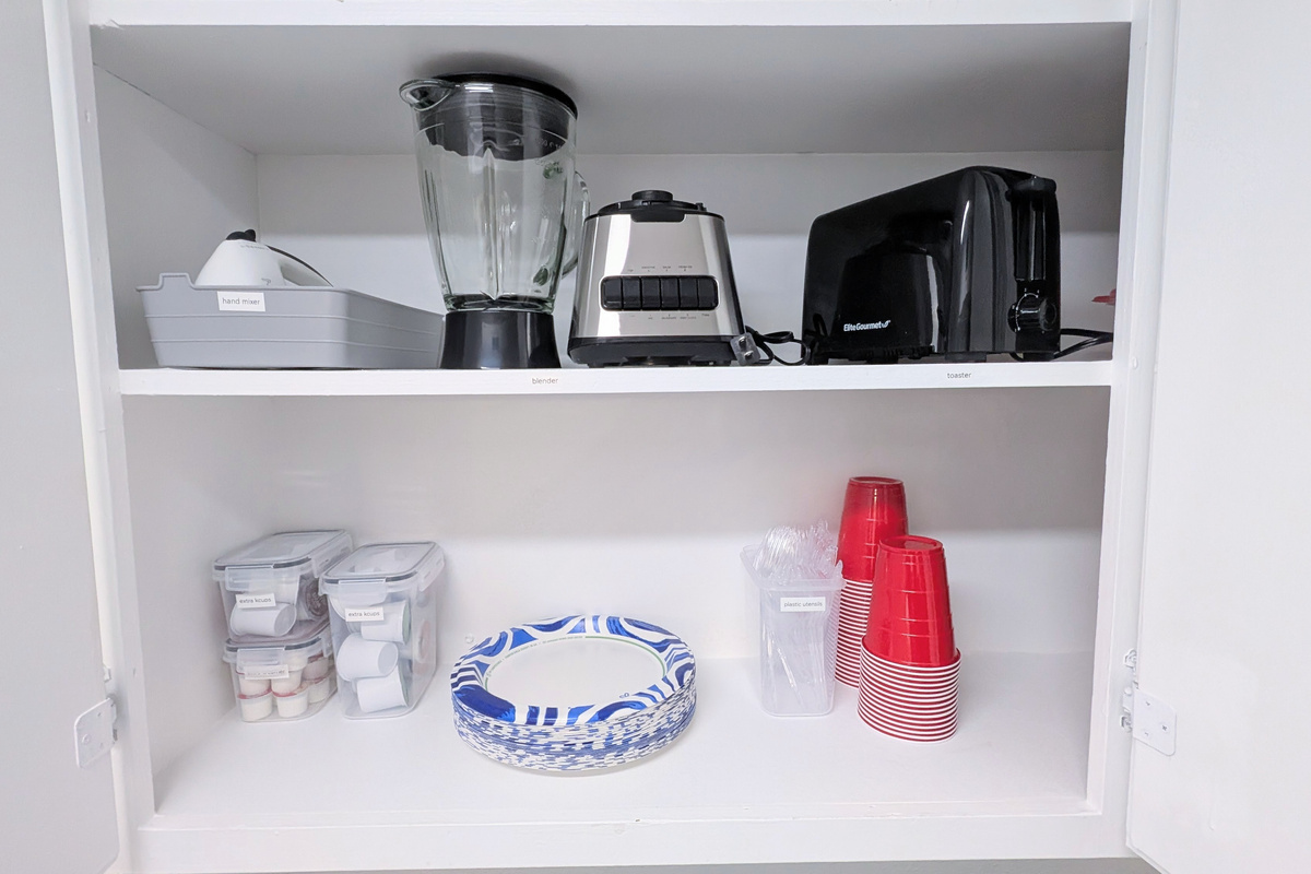 Small appliances, including a hand mixer, blender, and toaster, are provided, along with extra coffee supplies and disposable plates, utensils, and cups.