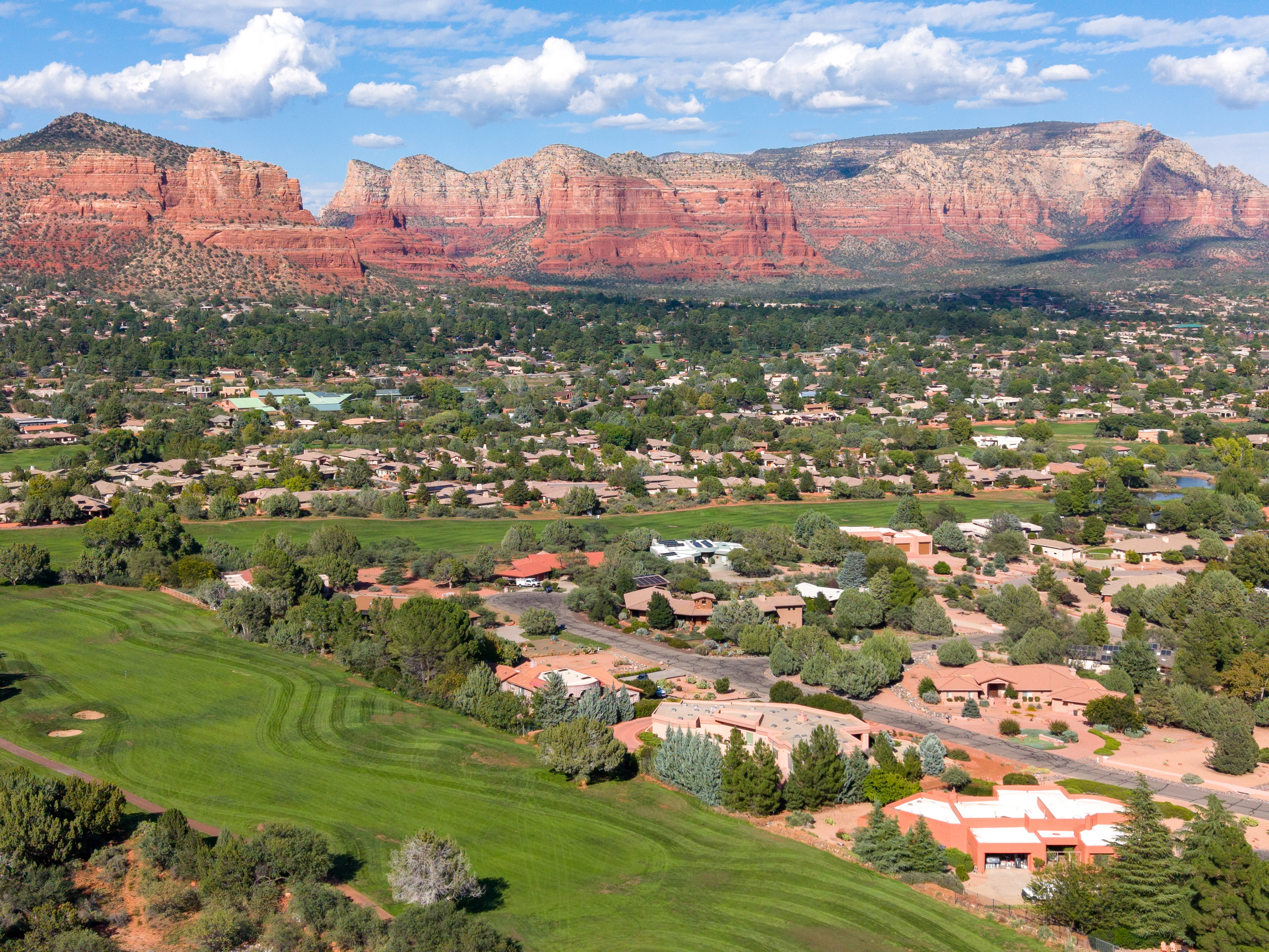 Breathtaking bird’s-eye views over lush golf fairways leading directly toward Sedona’s iconic red rock bluffs and blue skies.