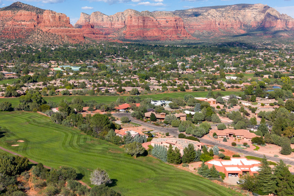 Breathtaking bird’s-eye views over lush golf fairways leading directly toward Sedona’s iconic red rock bluffs and blue skies.