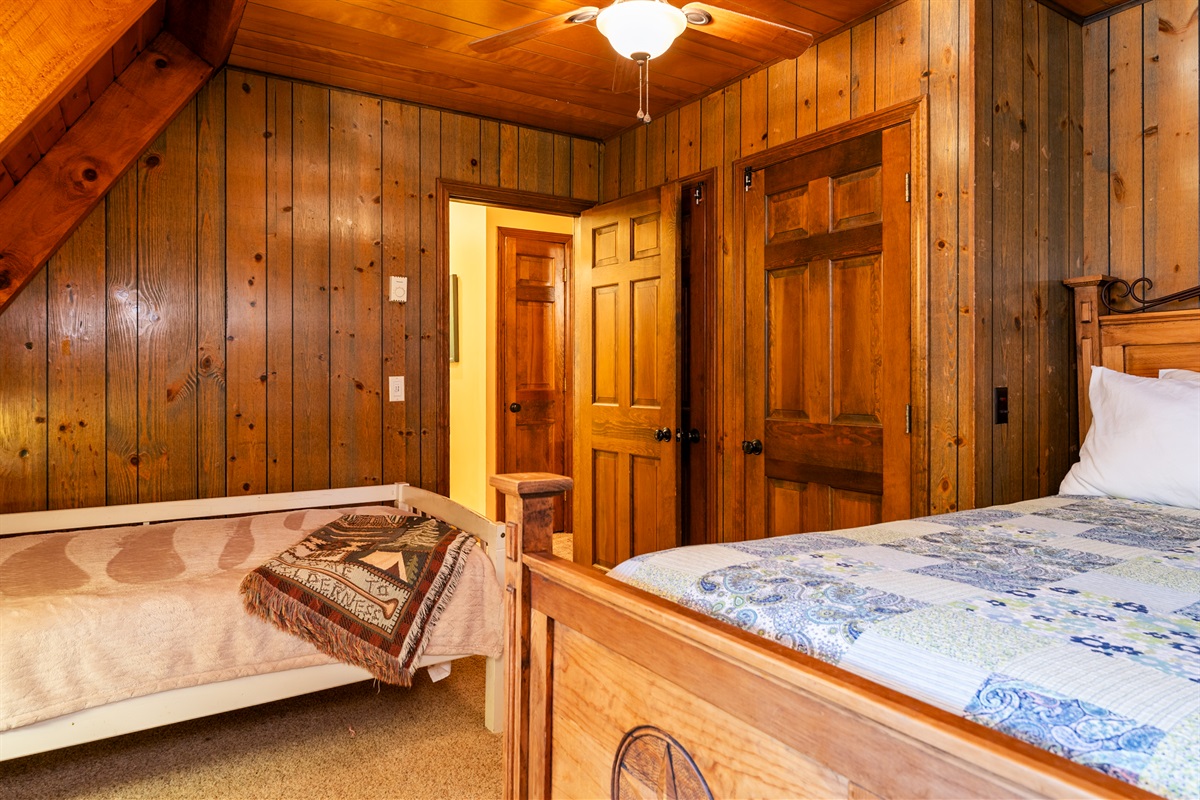 Bedroom #2 Charming log cabin bedroom with a queen bed and twin bed, natural wood beams, and bright windows showcasing forest views.