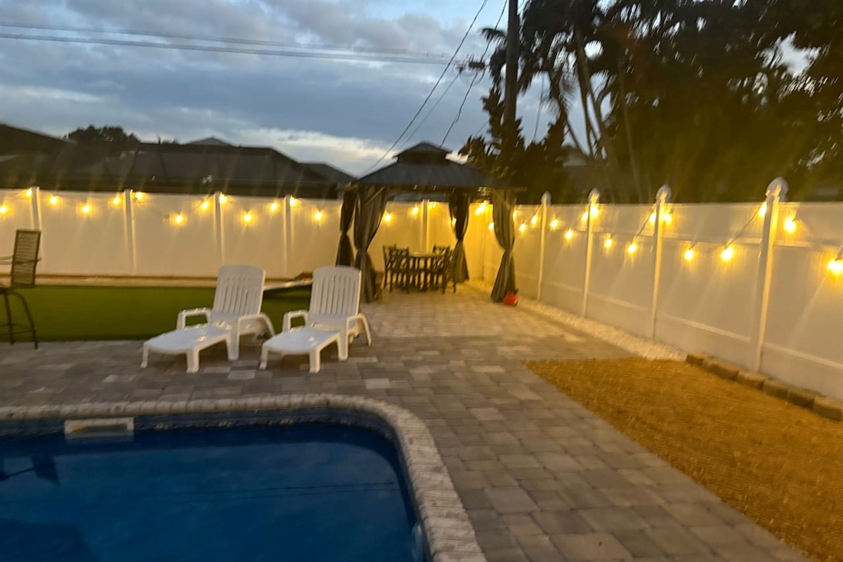 Pool area in the evening when the lights are on gazebo and launge chairs 