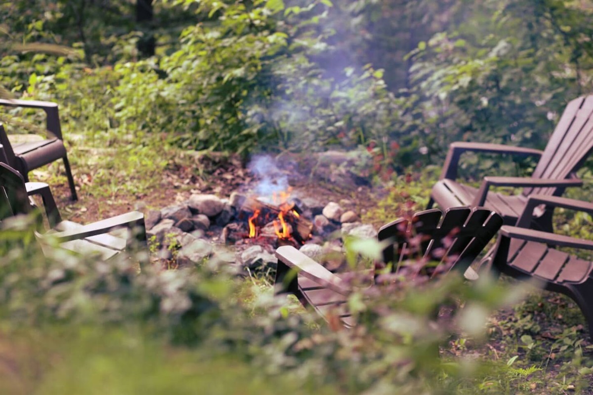 Fire pit and outdoor seating on lawn area above Lac McArthur; firewood is provided for your use
