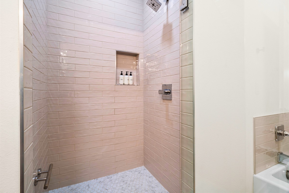 Modern walk-in shower with tiled walls and luxury bath essentials provided.