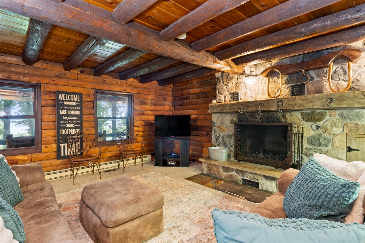Charming log cabin living room featuring exposed beams, a grand stone fireplace, and plush seating for ultimate relaxation.