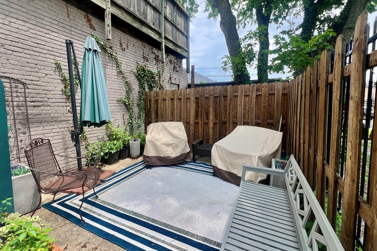 Private patio retreat with seating area, protective furniture covers, and lush greenery along the wall