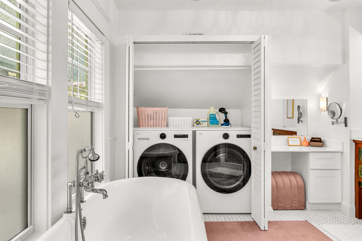 Full Bathroom #1: Elegant ensuite bath featuring an antique clawfoot soaking tub, modern glass-enclosed shower, built-in dressing table with magnifying mirror, and full-size washer and dryer tucked behind double doors.