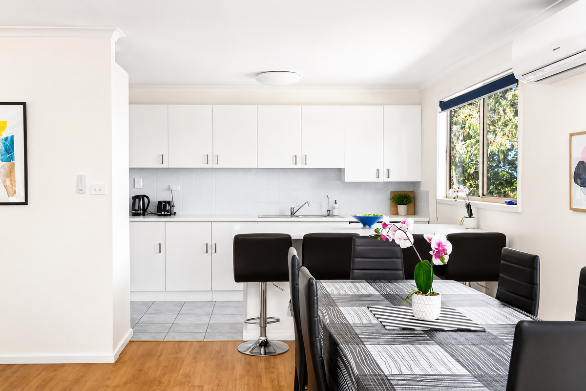 The open kitchen and dining area at Carlenes Getaway keeps meals easy, with reverse-cycle comfort and a leafy Loch Sport outlook from the window.