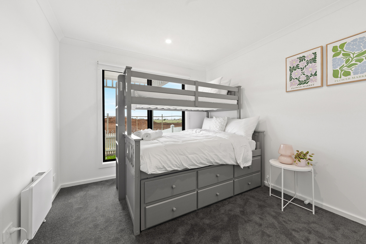 Bunk bed with a double below and a single above, ladder and under-bed drawers, made up with linen, beside a window and framed art.