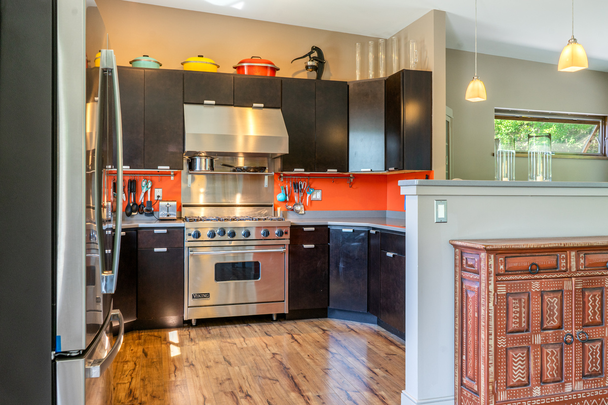 Fully stocked gourmet kitchen featuring a professional Viking range and modern black cabinetry with a bold orange backsplash. Enjoy expansive granite countertops and stainless steel appliances, perfect for preparing meals after a day in Acadia.