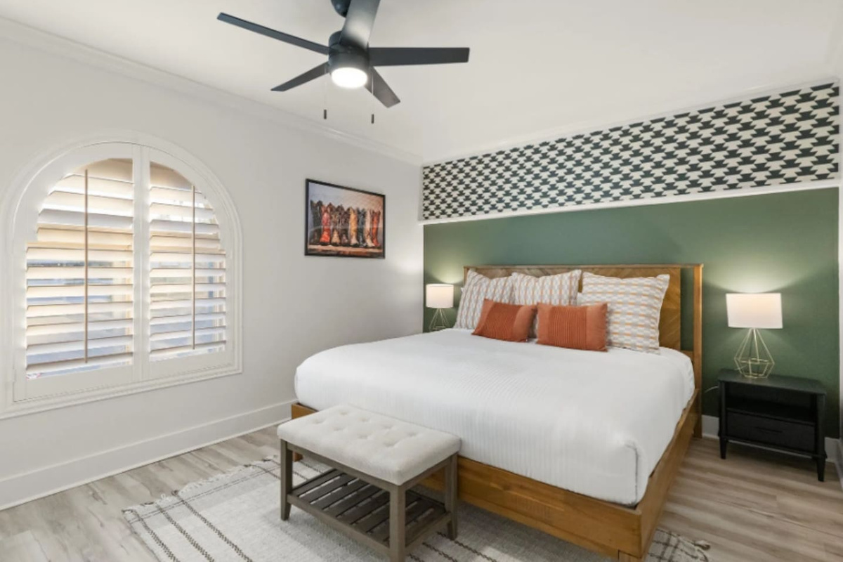 A houndstooth accent and rich green wall frame the king bed, with a playful boot print nodding to the western spirit throughout the home. Arched shutter windows and warm bedside lighting round out a room that feels both cozy and stylish.
